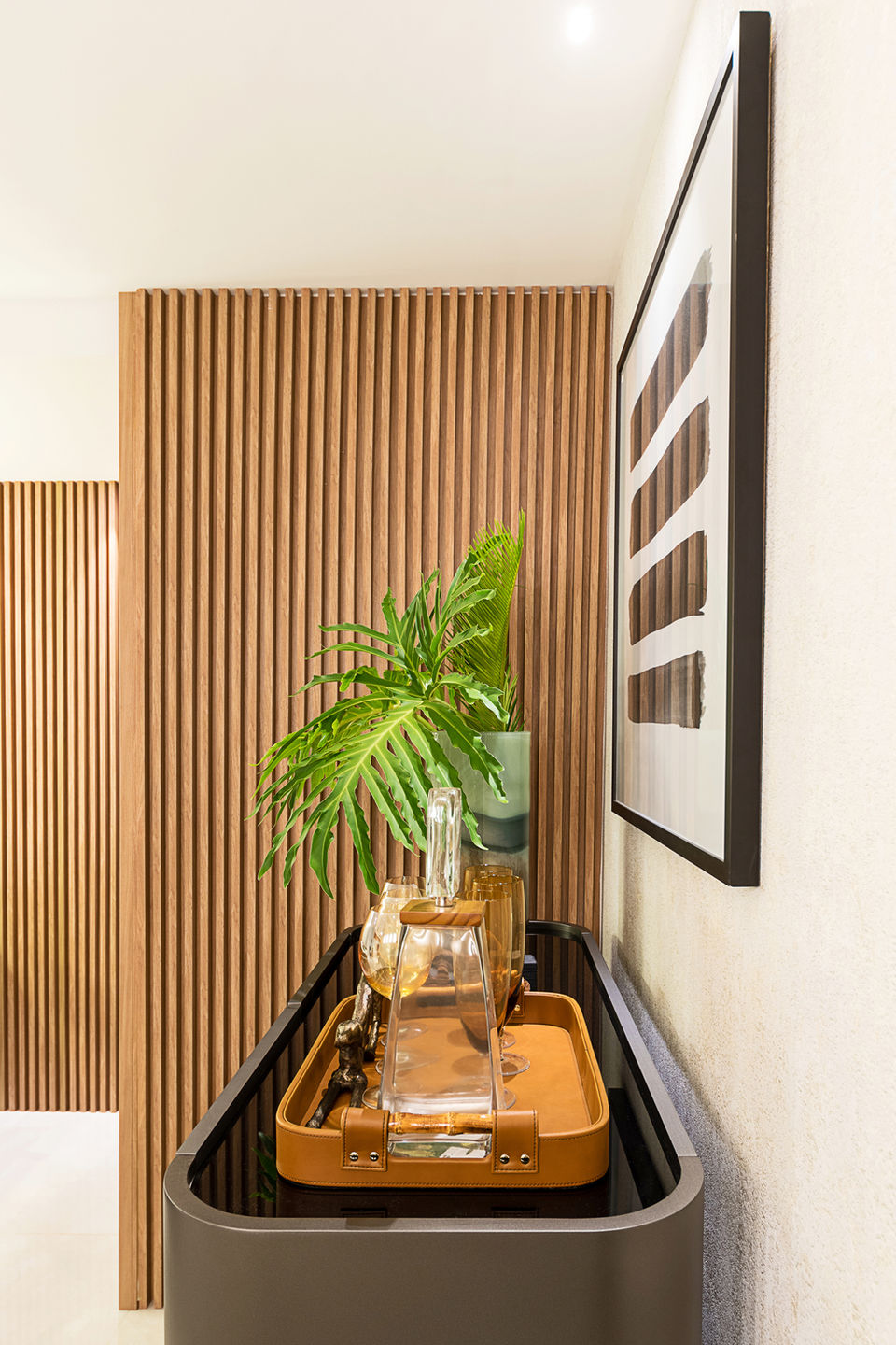 Sala de jantar contemporânea com painel ripado de madeira, mesa retangular com cadeiras em tom amadeirado, iluminação pendente moderna e aparador com decoração elegante. Ambiente sofisticado, integrado ao living, com design de interiores clean e aconchegante.