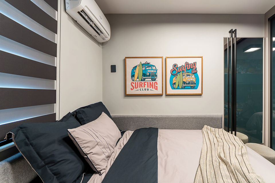 Quarto juvenil com cama de solteiro, marcenaria azul e cinza, escrivaninha com cadeira acrílica e iluminação de tarefa. Persiana horizontal dupla, ar-condicionado e decoração com pôsteres e objetos personalizados. Projeto funcional com layout compacto e estilo contemporâneo.