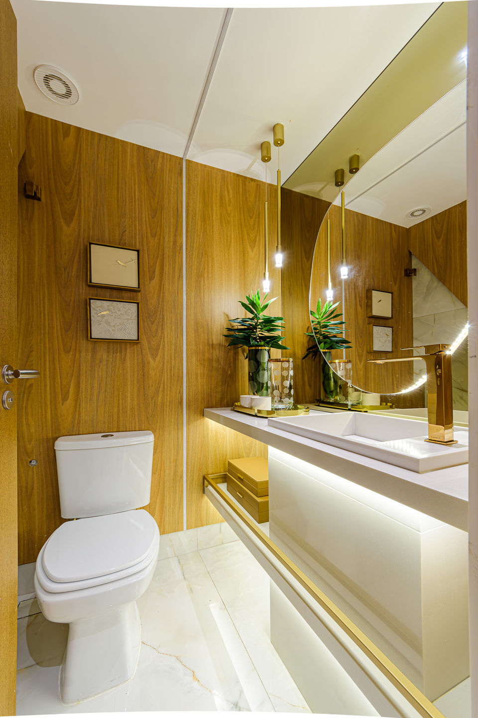 Lavabo com revestimento em painel amadeirado, bancada branca com iluminação embutida, espelho orgânico iluminado e metais dourados. Destaque para o design contemporâneo, detalhes elegantes e atmosfera acolhedora.