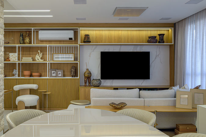 Ambiente integrado de estar e jantar com paleta neutra, mobiliário contemporâneo, mesa redonda laqueada, cadeiras estofadas e pendente escultural em madeira. Destaque para o aparador com iluminação embutida e cortinas em linho que valorizam a luz natural.