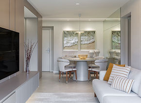 Sala de estar integrada à varanda em tons neutros, com sofá claro, painel ripado em madeira, iluminação indireta e vistas para área verde.