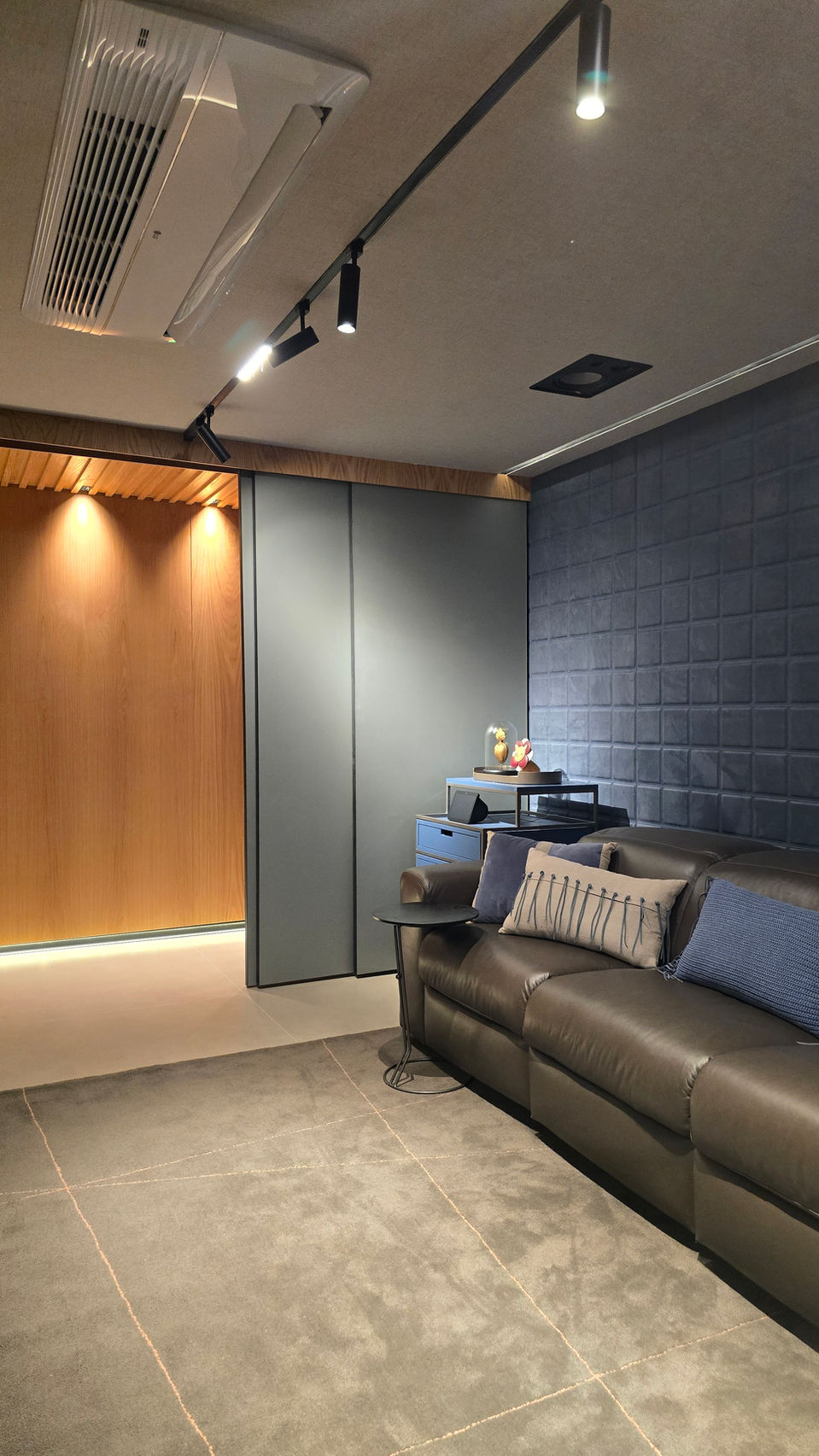 Sala de TV com iluminação técnica embutida, sofá retrátil em couro, painel em textura escura e marcenaria planejada. Ambiente acolhedor, funcional e ideal para momentos de entretenimento.