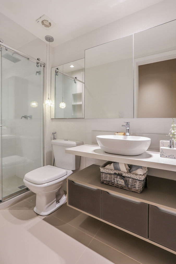 Banheiro com cuba de apoio, bancada branca, armário suspenso em tom taupe, pendentes decorativos e boxe com vidro transparente. Design leve e funcional em apartamento de alto padrão.