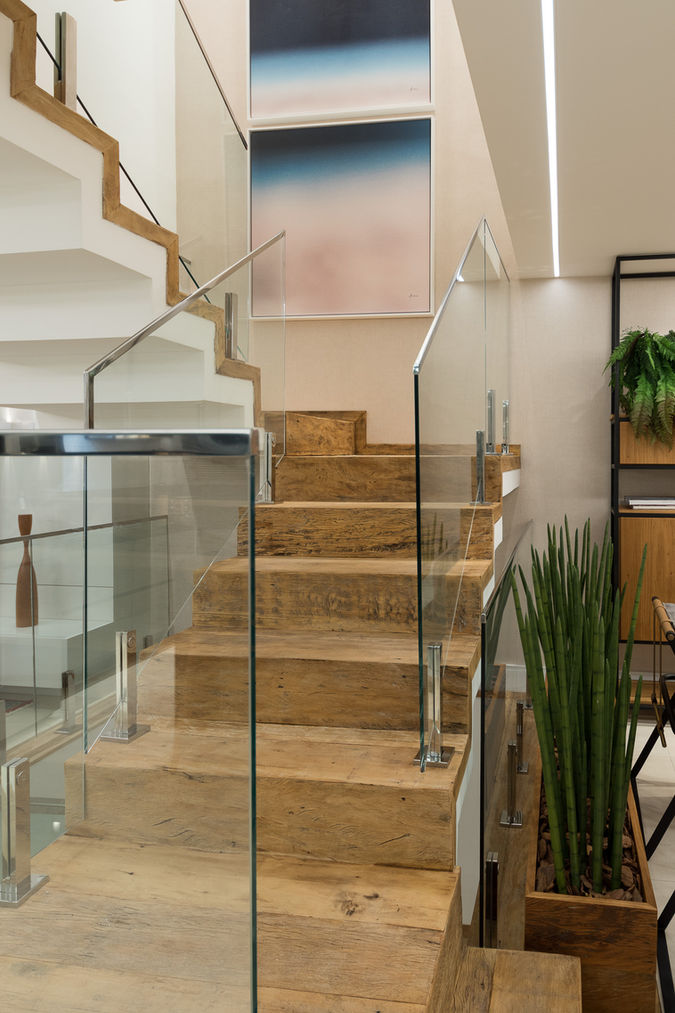 Escada em madeira de demolição com guarda-corpo em vidro e estrutura metálica, integrada a um ambiente contemporâneo com paisagismo interno e obras de arte minimalistas.