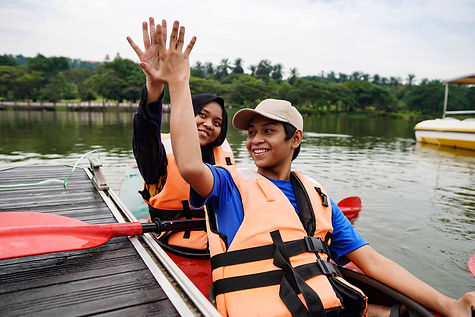 Two kids high-fiving in a canoe next to a dock