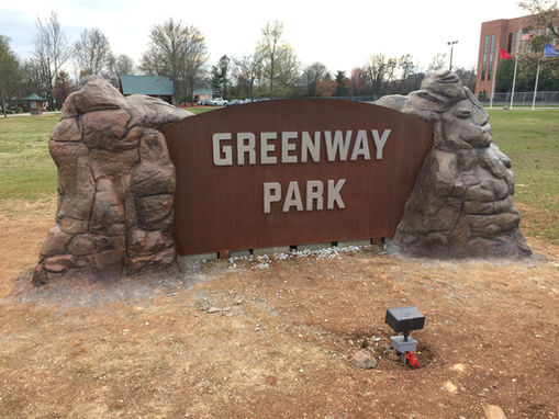 A rusted metal sign embedded in a large sculpted rock reading "greenway park".