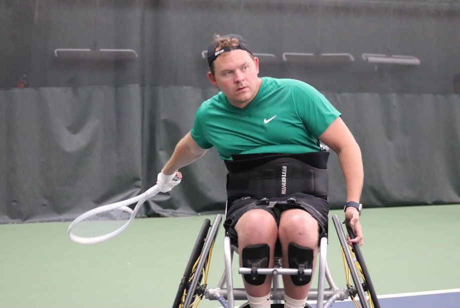 Wheelchair tennis athlete prepares to hit tennis ball back to opponent.