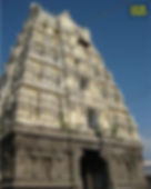 Ornate temple tower with intricate carvings against a clear blue sky. The structure is gray and cream, adding to its majestic appearance.Yathothkari Perumal Temple