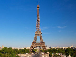 Eiffel Tower under a clear blue sky, surrounded by green trees and cityscape. "TOUR TIMES" text in the top left corner. Peaceful mood.Europe Tour From India
