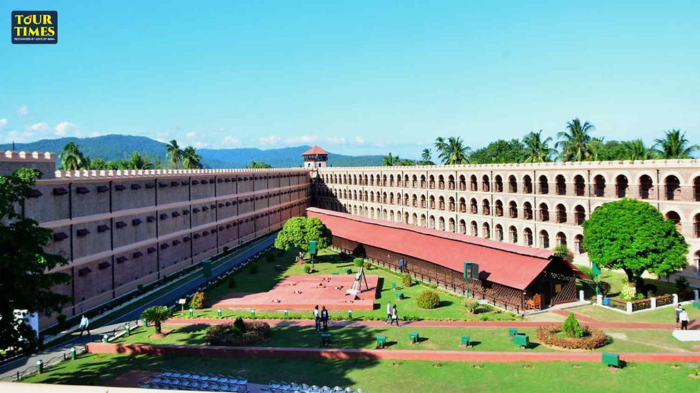 Colonial-era prison with red roofs and arches, set in lush green gardens under a clear blue sky. People walk through the courtyard.