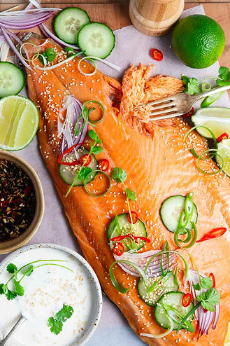 Whole side of smoked salmon on a board surrounded by sauces, herbs and sesame seeds