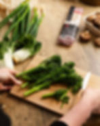 Hands holding a wooden chopping board with green vegetables