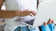 Junge Frau mit weißen T-Shirt und Jeans surft stehend mit ihren Laptop im Internet.