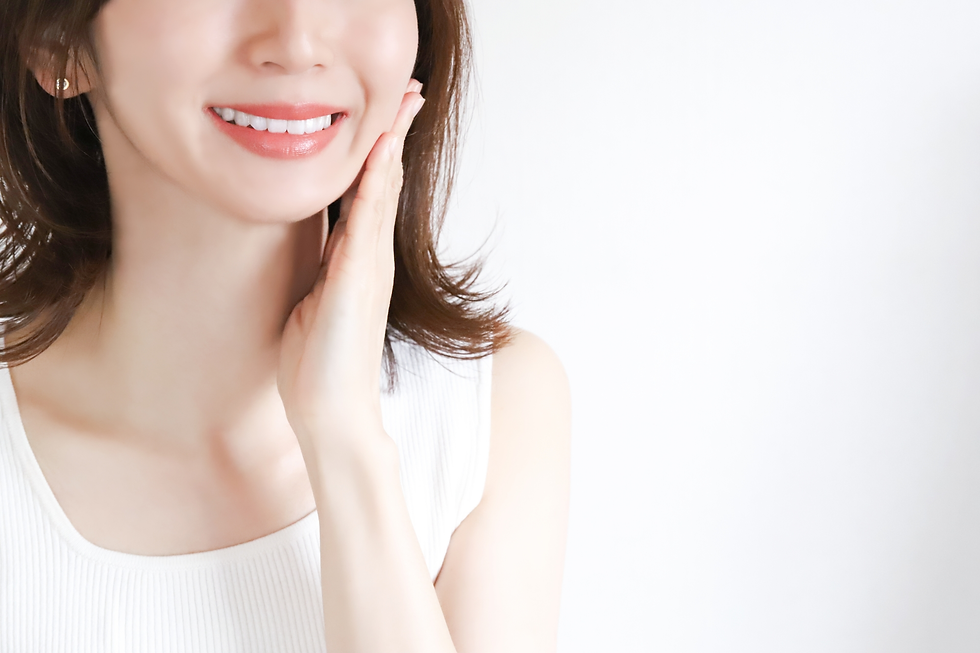 A young Asian woman smiling and gently touching her cheek with one hand, showing clear and healthy-looking skin
