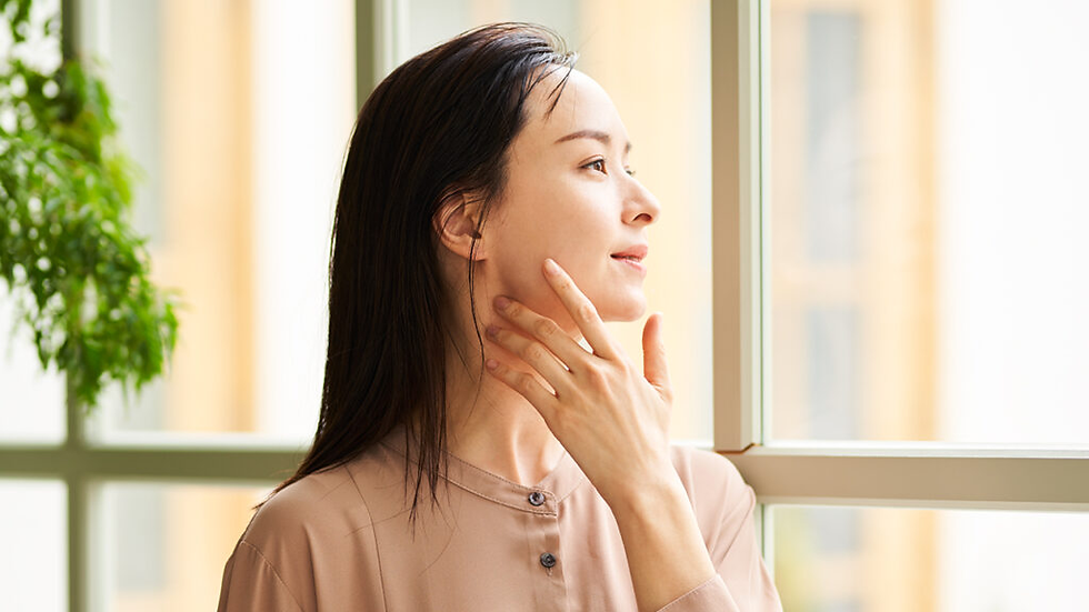 A woman gently touching her face while looking out a window