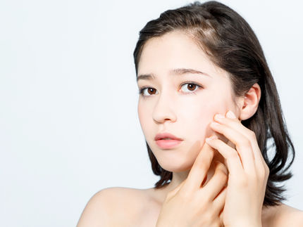 Woman touching her cheeks while examining her skin, concerned about acne marks vs acne scars