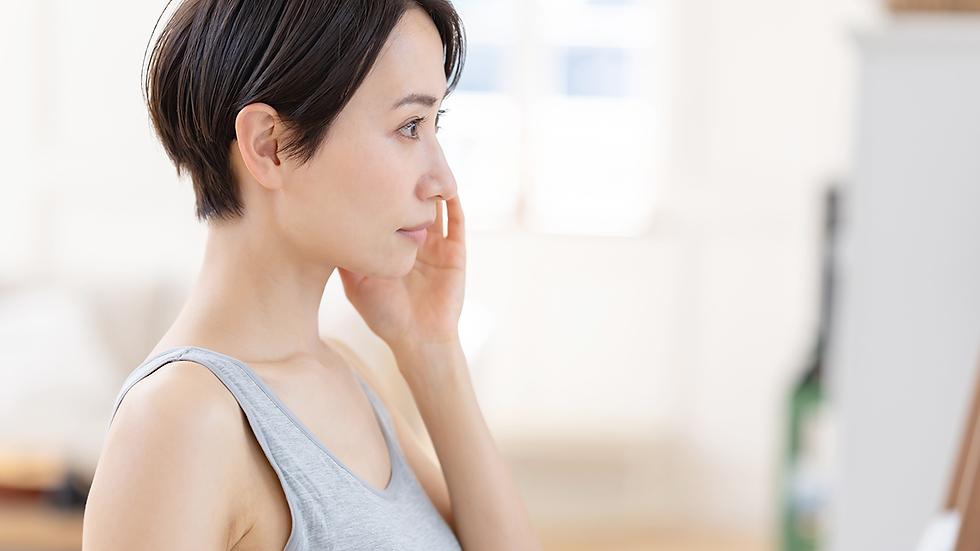 A woman with short hair gently touching her cheek while looking forward in a bright room