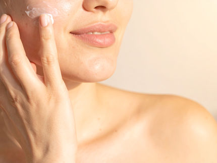 Close-up of a smiling woman applying niacinamide cream to her cheeks, focusing on the lower half of the face.