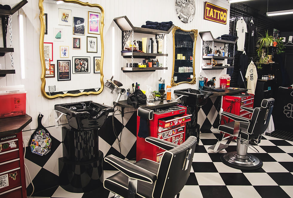 Hair Salon & Barbershop interior with black chairs, red tool drawers, gold-framed mirrors, tattoo sign, and art on walls. Black and white checkered floor.