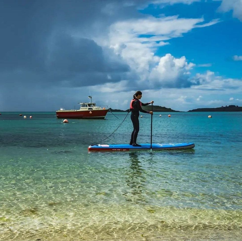 A woman is paddling a paddleboard and is wearing a leash attached to her buoyancy aid