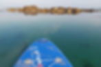 A rocky ledge in a calm sea with a paddleboard in the foreground