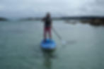 A woman is on a paddleboard with the shoreline of St Martin's on the right