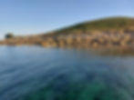 The shoreline of St Martin's showing clear water and a rocky shore with Cruther's Hill in the background
