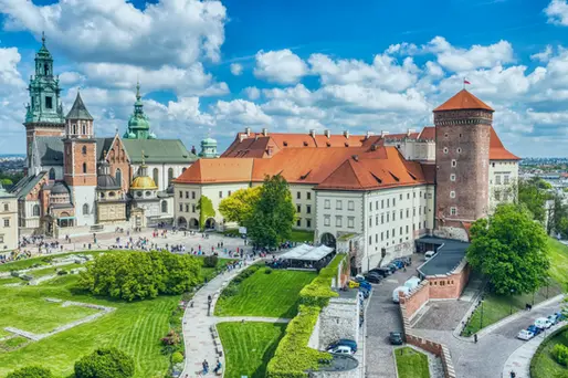 Wawel Castle and Cathedral complex overlooking the Vistula River in Kraków, Poland, with historic towers and red rooftops under a blue sky