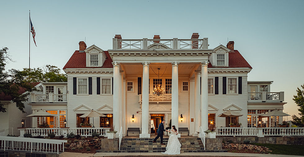 Elegant mansion with white columns and red roof at sunset. A couple in wedding attire stands on the steps, creating a romantic scene.