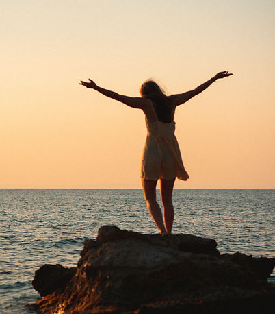 girl in summer dress holds hans in the air and dances on rock by the sea during sunrise_ed