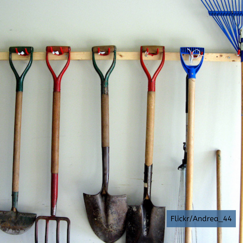 Large garden tools rakes and shovels hang in garage