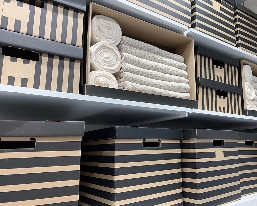 Shelves of black-and-tan striped storage boxes, with open boxes revealing neatly rolled white towels and blankets.