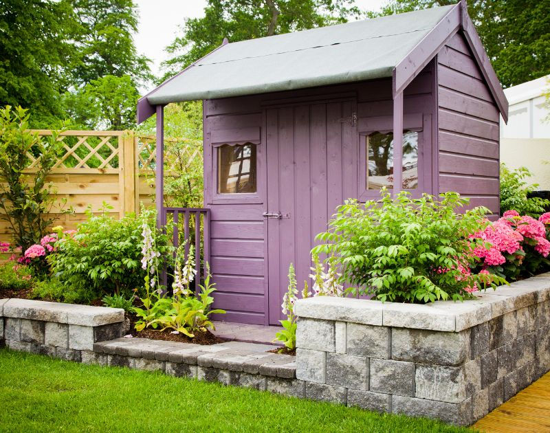 Stylish storage shed surrounded by colorful flowers. #backyarddecluttering #outdoororganization