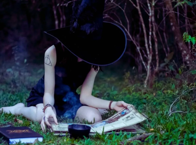 A young, beginner witch studies a book while sitting in nature