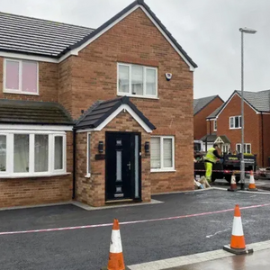 A new black tarmac driveway on a housing estate, cordoned off with traffic cones