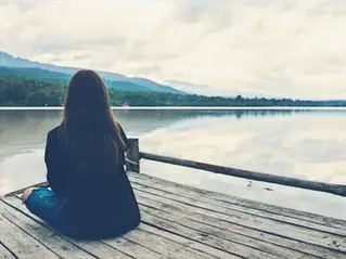 Eine Frau, die an einem See sitzt umgeben von Bergen