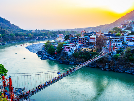 Rishikesh am Ufer des Ganges bei Sonnenaufgang mit der berühmten Hängebrücke Lakshman Jhula im Vordergrund