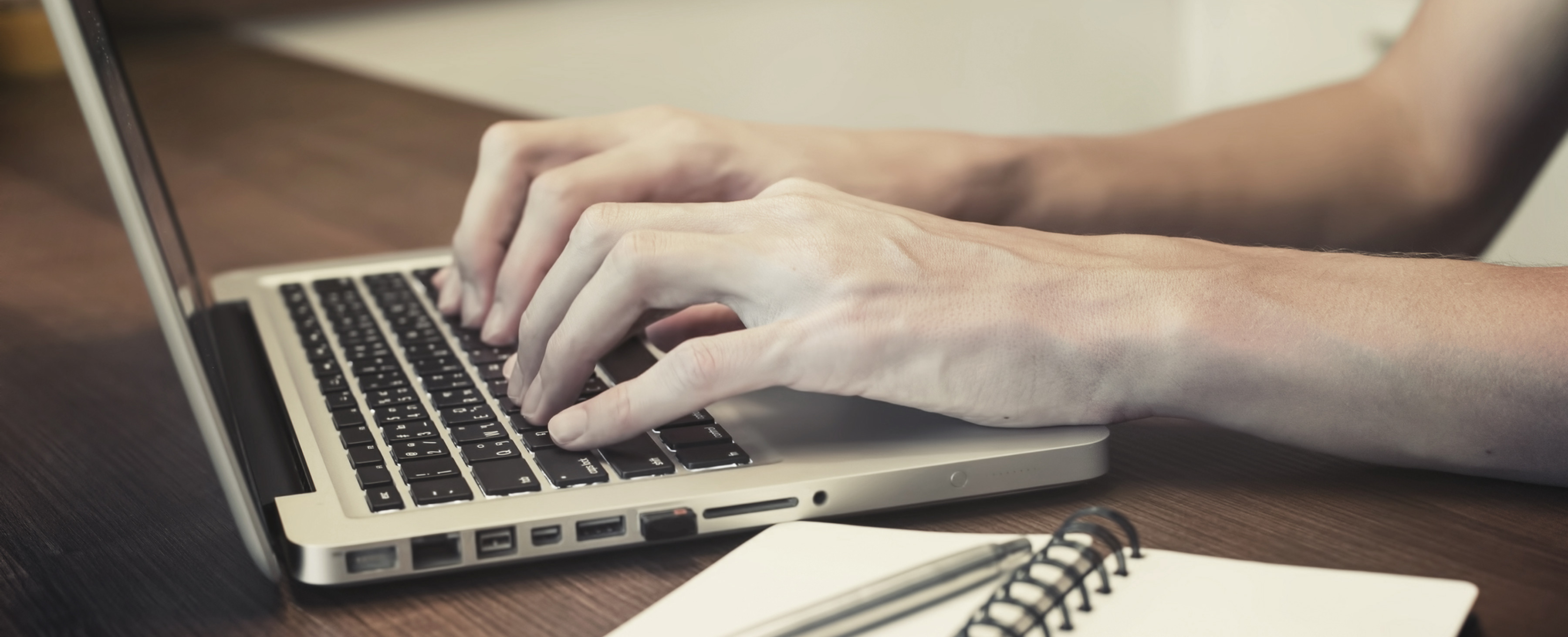 Close-up of a person typing on a laptop keyboard at a desk, illustrating repetitive hand movements that trigger carpal tunnel syndrome symptoms.