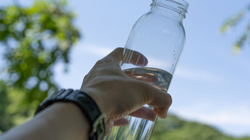 熱中症対策のための水分補給。透明なボトルを持つ手。背景に青空と緑の木々が見える。リラックスした雰囲気が漂う、明るい自然の風景。