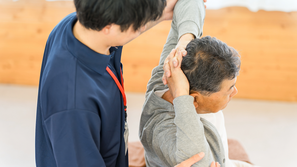 リハビリが青い制服を着て、年配男性の腕を支えストレッチをサポートする。転倒予防。