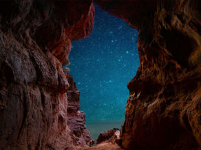 A star filled sky displayed through and opening in a red-rock formation