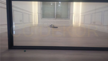 The reflection of the empty room with its wooden floor is visible in the black-framed glass with wall trim.