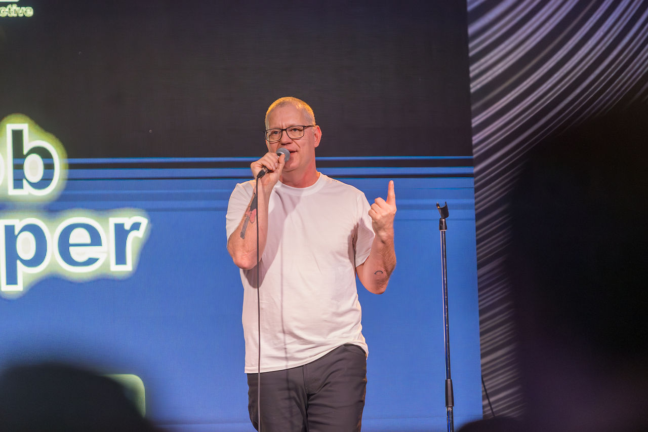 Comedian performing on stage under bright spotlights, making the audience laugh.