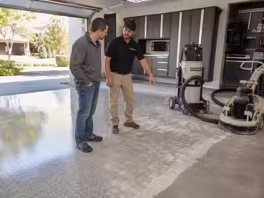 Homeowner discussing epoxy garage floor installation with contractor showing coated garage floor and surface preparation process