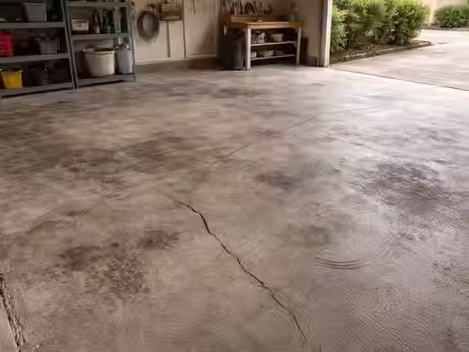 Uncoated garage floor with visible cracks, stains, and surface damage showing long-term wear