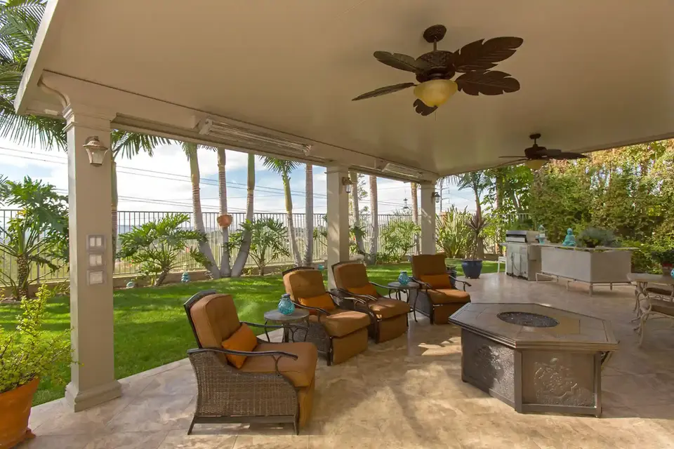 Relaxing patio with four lounge chairs, ceiling fan, and fire pit, overlooking a lush green lawn.