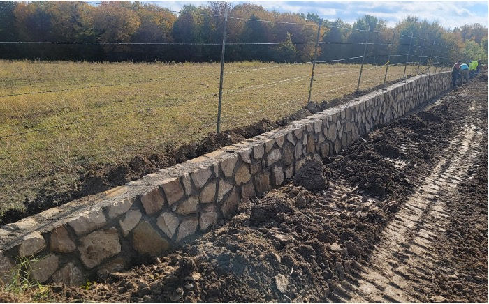 Rustic stone wall under construction near fence