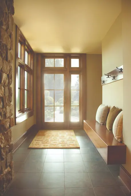 Sunlit entryway with bench, pillows, and coat hooks