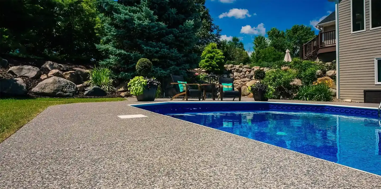 Stunning poolside view: Pebble-textured deck, inviting pool, and lush landscaping