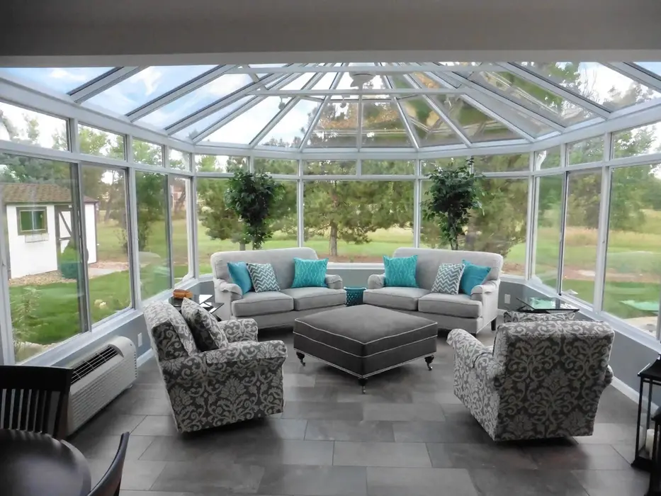 Sunroom interior: gray couches, ottoman, and patterned armchairs near large windows